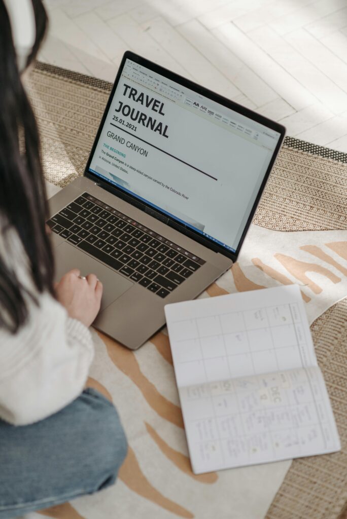 pexels-photo-7120921-7120921-1 A young woman plans a travel journal using a laptop and notebook indoors on a cozy rug.